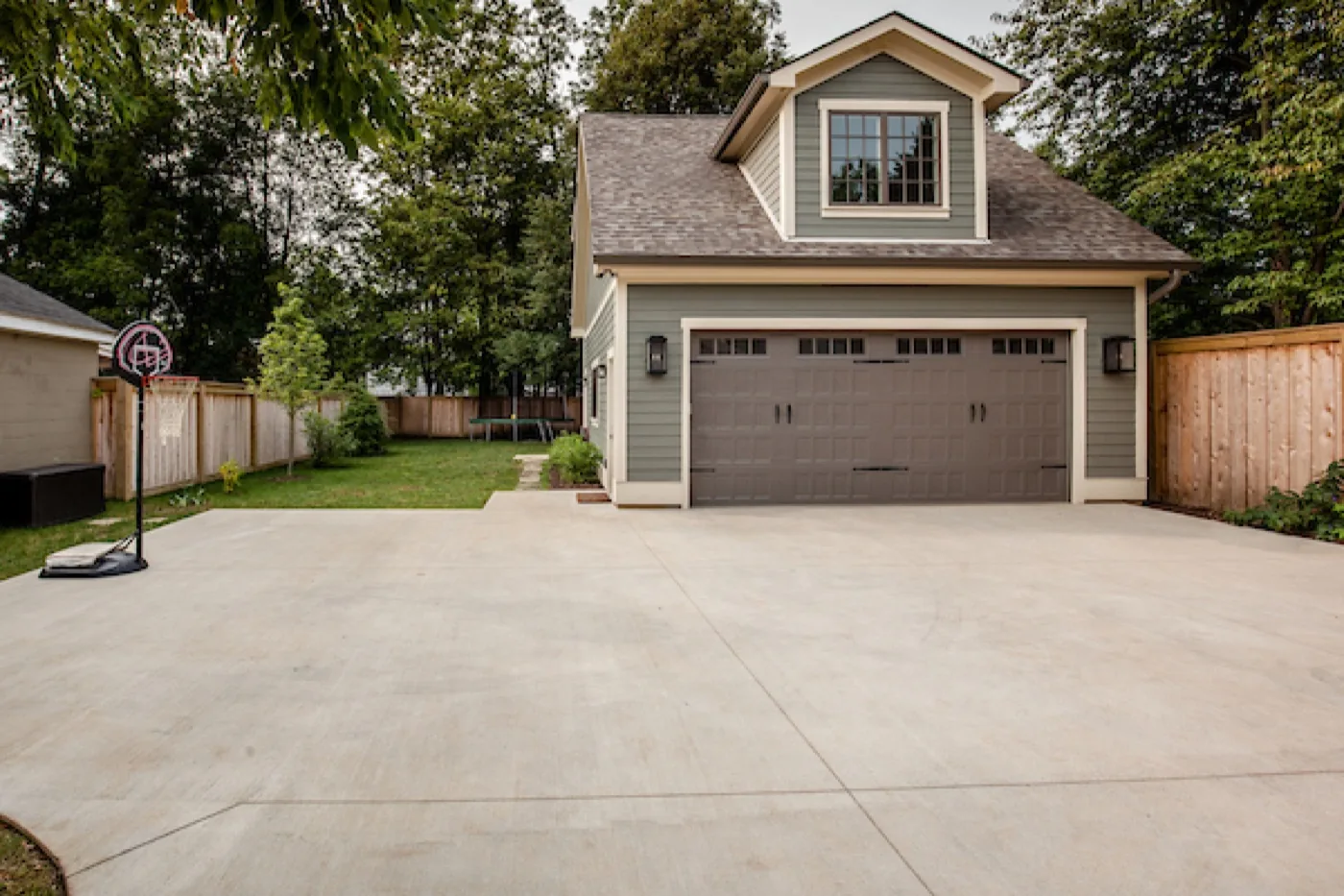 A detached garage addition with a dormer, matched siding and a poured drive